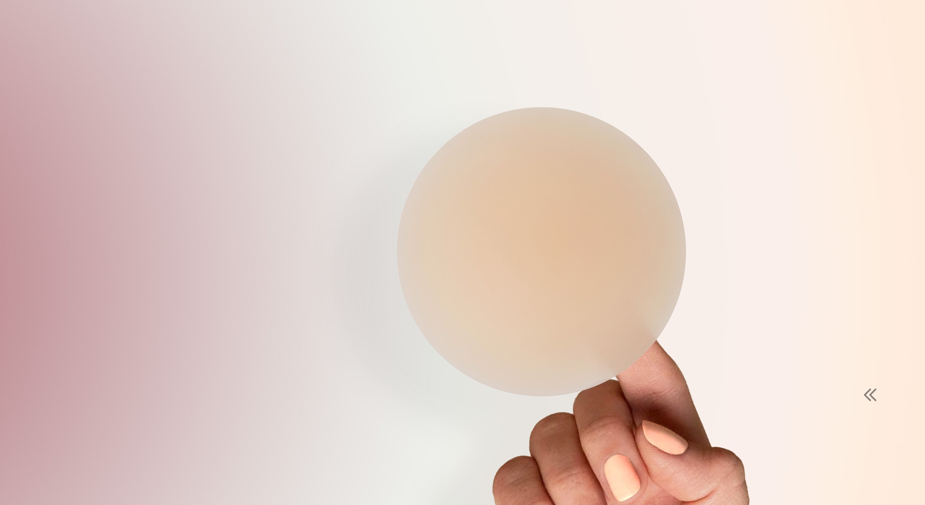 Hand holding a Bare & Basic Vanish premium reusable nipple cover against a gradient background